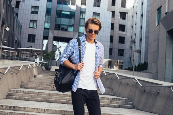 Modern street style. Handsome young man in sunglasses looking away while walking outdoors