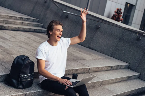 Hey ben buradayım! Yakışıklı genç adam onun laptop kullanarak ve açık havada otururken gülümseme ile el hareketi