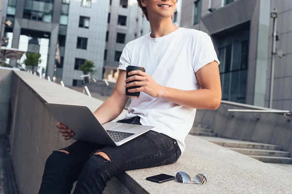 Coffee and study  what can be more? Part of young man using his laptop and drinking coffee with smile while sitting outdoors