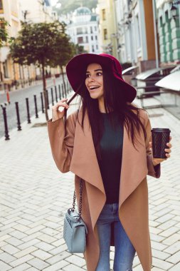 Sonbahar söyleyen sıkıcı mı? Güzel genç kadın şık şapkanı ve paltonu uzakta ayakta açık havada süre gülümseme ile seyir