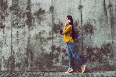 A gitmek mükemmel kahve molası. Cep telefonu üzerinde konuşurken ve kahve fincanı duran beton arka plan açık havada tutan güzel genç kadın yan görünüm 