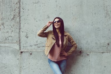 Güneş shinning ve havanın güzel olduğu. Güzel genç kadın uzak gülümseme ile seyir ve gözlüklerini beton arka plan açık havada duran ayarlama 