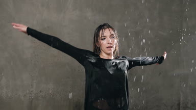 Islak dansçı siyah elbise ve stüdyo su damlaları altında kendini daireler. Modern dans. Yağmurda dans