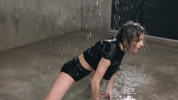 Mujer húmeda bailarina en traje de cuerpo negro y puntos realiza danza moderna en el suelo bajo la lluvia y salpicaduras de agua. La chica que bailó bajo el agua durante el baile en el suelo en interiores — Vídeos de Stock