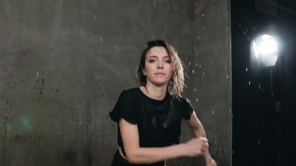 Влажная танцовщица в черном теле совершает прыжок под дождем и брызги воды. Танцовщица, которая танцевала под водой во время танца на сцене, смотрит в камеру — стоковое видео