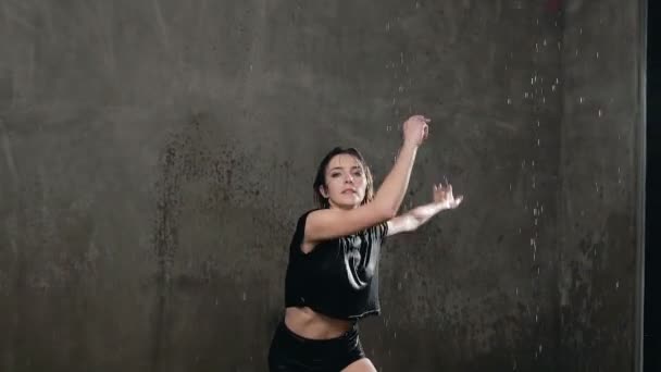 Natte meisje danser in zwart lichaam voert een sprong in de regen en spatten van water. De danser die onder water tijdens de dans op het podium danste gekeken naar de camera — Stockvideo