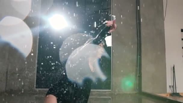 Una giovane ballerina esegue una danza contemporanea sotto la pioggia d'acqua in studio. Una ballerina che balla danza attiva in acqua con spruzzi nel fascio di un riflettore — Video Stock