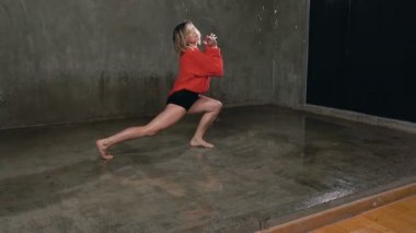Profesyonel bir dansçı bir stüdyo ışık önünde sahnede bir modern dans su yağmur altında gerçekleştirir. Örme kırmızı kazak ve siyah şort stüdyoda bir çağdaş dans dansçı gerçekleştirir