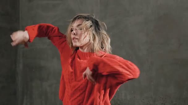 Hermosa bailarina bailando danza moderna en suéter rojo y pantalones cortos negros bajo las gotas de agua en el estudio antes de la luz del estudio. Danza moderna. Baila bajo la lluvia — Vídeos de Stock