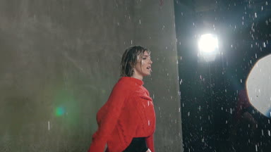 Islak sarışın kız kırmızı kazaklı arka planı gri bir duvar Studio'da yağmur damlaları altında dans. Islak kadın dansçı atlama unsuru içinde dans yağmur sırasında gerçekleştirir