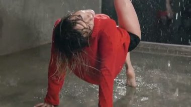 Kırmızı kazaklı ıslak dansçı stüdyo ışık ve su yağmur thew katta dans ediyor.