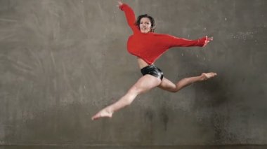 Kırmızı kazaklı ıslak kadın dansçı bir sıçrama yağmur ve su sıçramalarına gerçekleştirir. Sahnede dans sırasında suyun altında dans dansçı kız kameraya benziyor