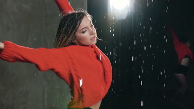 Genç profesyonel kadın dansçı akrobatik dans Studio su yağmur altında gerçekleştiriyor. Kırmızı kazak ve şort çağdaş tarzda su damlaları, sahnede dans spor kız yakın