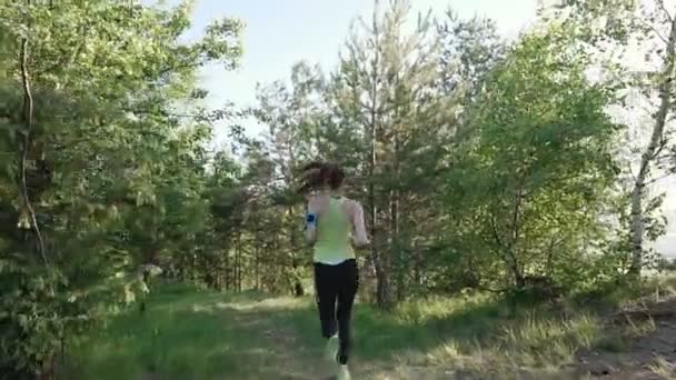 Vista trasera. Corredor mujer joven corriendo en el parque haciendo ejercicio al aire libre rastreador de fitness tecnología usable. Atleta chica corriendo en el parque que huye de la cámara y escuchar música en los auriculares en un — Vídeo de stock