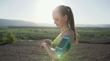 Hızlı bir telefon kol bandı gösteren smartphone dokunmatik ekranlı dağda günbatımında giyen hızla kaçan fitness atlet kız. Müzik koşucu. Kardiyo egzersiz