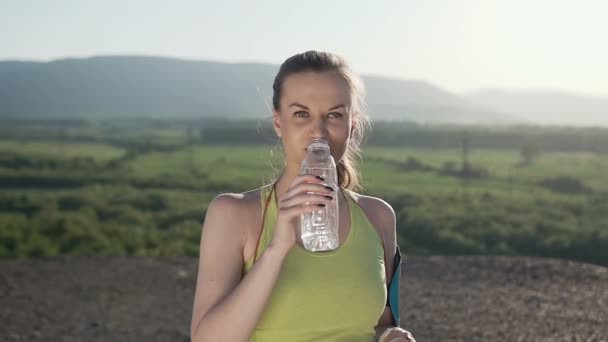 Attraktive Sportlerin, die kaltes Wasser trinkt, nachdem sie an sonnigen Tagen im Berg an der frischen Luft gelaufen ist. schöne Fitness-Athletin trinkt Wasser nach dem Training, Gesundheit und Sport — Stockvideo