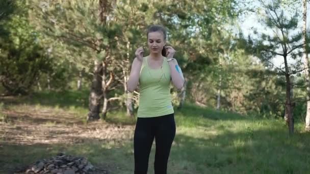 Młoda kobieta słuchanie muzyki za pomocą słuchawek na aplikację smart phone dla fitness motywacja. Sportowiec dziewczynka runner w sportowej uruchomiona na przyrody w parku na zachód słońca — Wideo stockowe