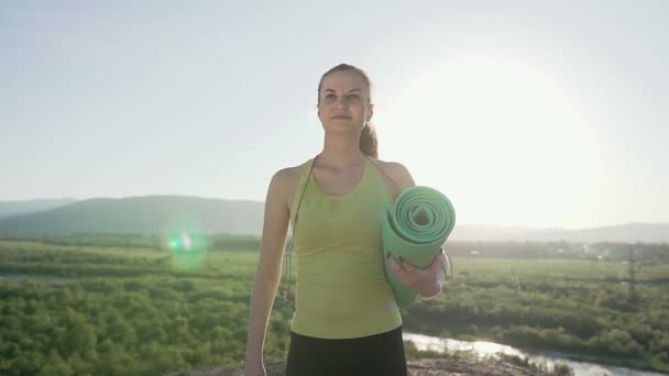Молодая спортсменка ходит на утреннюю тренировку на свежем воздухе. Крупный план здоровой красивой девушки йоги с ковриком на улице в общественном парке — стоковое видео