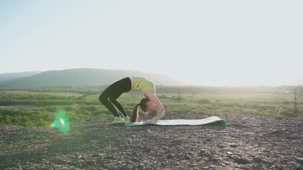 Yoga - Gymnastisk tjej göra utöva utbildning i toppen av berget i floden bakgrunden nära skogen. Flexibilitet utöva utbildning. Vältränad ung kvinna som värmer upp stretching i utomhus på solnedgång eller soluppgång — Stockvideo