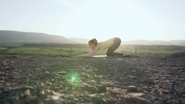 Йога - гимнастическая девушка делают упражнения на вершине горы на речном фоне возле леса. Гибкость тренировки упражнения. Подходит молодая женщина, разогревающаяся на свежем воздухе на закате или восходе солнца — стоковое видео