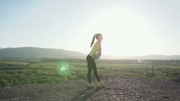 Jeune femme sportive faisant de l'exercice de yoga ouvrir son tapis de yoga vert en plein air en montagne. Fille en vêtements de sport ouvre un tapis vert pour l'entraînement yoga — Video