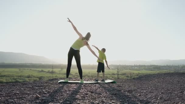 Arkadan Görünüş anne ve oğlu gündoğumu veya günbatımı dağ tepesinde spor egzersizleri yapıyor. Atlet aile kız ve erkek kardeş spor bir egzersiz açık üzerinde dağda gerçekleştirme — Stok video