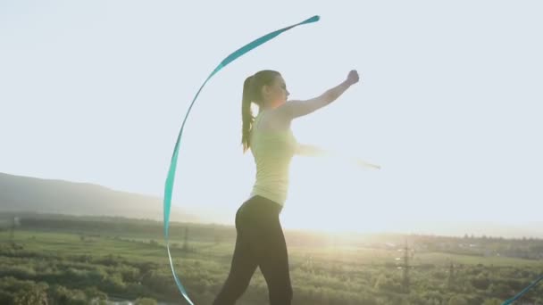 Attraktive Turnerin, die mit Schleife oben auf dem Berg im Sonnenuntergang tanzt. Rhythmische Sportgymnastin. Sportlerin — Stockvideo