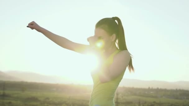 Junge Frau boxt mit Schatten auf dem Gipfel des Berges bei Sonnenuntergang. Sportmädchen im Nahkampf, Sportboxen bei Sonnenuntergang. Boxtraining im Freien — Stockvideo