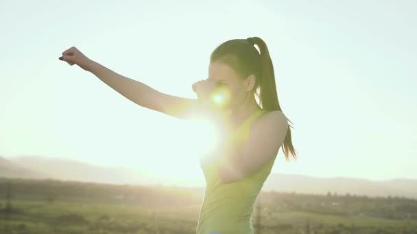 Une jeune femme pratique la boxe à l'ombre sur le sommet de la montagne au coucher du soleil. Fille de sport engagée dans le combat de mêlée, boxe sportive au coucher du soleil. Entraînement de boxe en plein air — Video