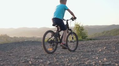 Dikiz dağlık bir alanda siyah Bisiklete binen bir çocuk. Çocuk Bisiklete binme. Genç çocuk yaz gün batımında banliyölerinde dağ yolda bisiklete binmek