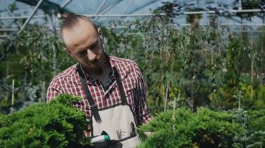 Yakın çekim bir fotoğraf makinesi üzerinde bir güzel genç bahçıvan binmek. Çiçekler ve ağaçlar su ile sulama bahçıvan, sakallı bir çocuktur.