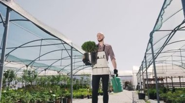 Genç bahçıvan sera gider, bir yeşil pot ve huni elinde tutar. Stabilize kamera hareketi, genel planı.