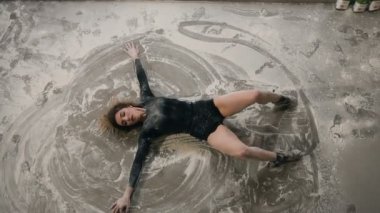 Üstten görünüm. Genç dansçı kız siyah vücut toz veya beyaz bir toz bulutu içinde katta modern dans dans takım elbise giymiş. Bir un yerde contemmporary dans gerçekleştirmek dansçı kız