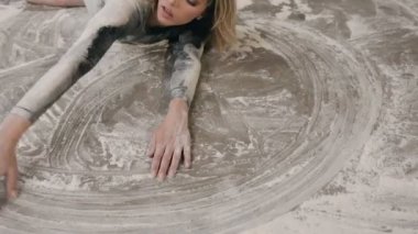 Siyah beden takım elbise giymiş genç bir kadın ile un ya da beyaz toz ve elini bir sanat bir daire bu toz veya un resim yapma kirli bir yerde yatıyor. Kız dansçı gerçekleştirmek