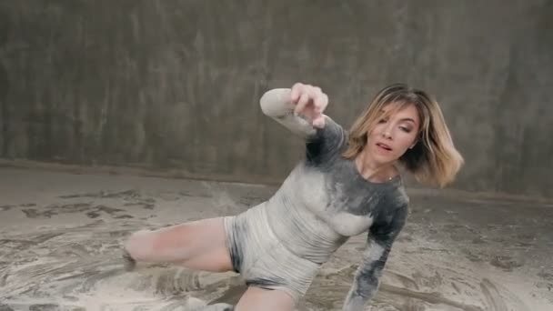 Жінка-танцівниця виконує танцювальну п'єсу на підлозі в білому пилі. Танцівниця виконує мистецький танець у чорній футболці, шортах та балеті на підлозі, забрудненій білим — стокове відео