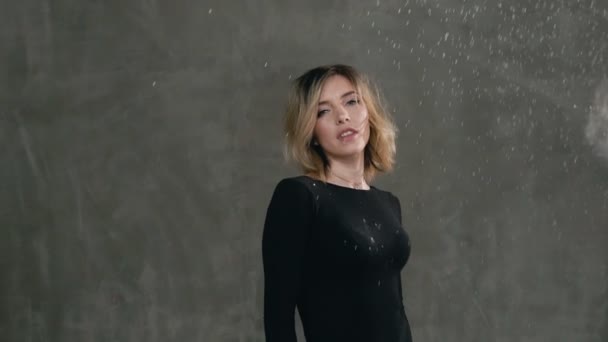 Cute girl standing on the background of a gray wall in the studio on which the grains of white powder or flour are shaken looking at the camera and smiles — Stock Video