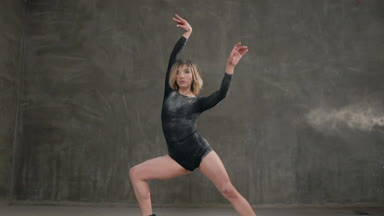 Siyah beden takım elbise giymiş güzel dansçı arka plan gri bir duvar üzerinde toz veya beyaz bir toz bulutu içinde dans pratiği yapıyor. Kadın dansçı gerçekleştirmek çağdaş dans stüdyosu