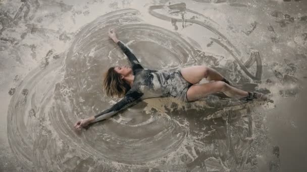 Vue de dessus. Danseuse habillée en costume noir danse sur le sol à l'intérieur nuage de poussière ou de poudre blanche. Danseuse qui exécutent la danse contemmporary sur le sol dans une farine ou de la poussière blanche dans — Video