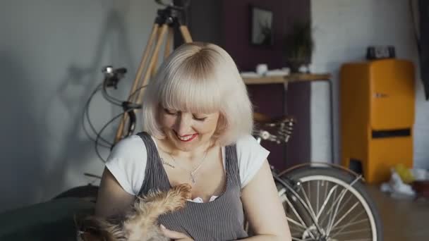 Kvinnan sitter på soffan i rummet spelar med lilla hund Yorkshire Terrier. En glad tjej som leker med en liten hund i hans rum, på bakgrunden av en cykel — Stockvideo