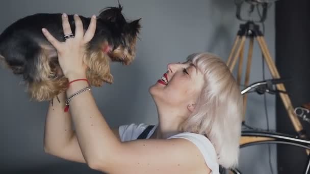 Chica rubia jugando con un perro. Lo lanza, lo presiona contra ella. El viento sopla sobre ellos. Todo sucede sobre un fondo gris . — Vídeos de Stock