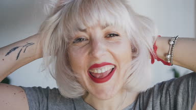 Çiller ile yakın çekim kız gülümsüyor ve kameraya benziyor. Sarışın saçları iki elimle dokunur ve içtenlikle gülüyor. 120fps