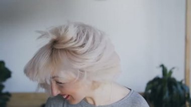 Kim kafasını dalgalar ve saçları beyaz bir duvar arka planı sallar çılgın sarışın yakın çekim portre. Güzel yumuşak ışık.