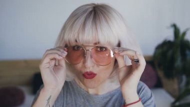 bir kadın şık gözlük Giydir, parlak ruj ve bukleler üzerinde sarı saçlı Genç ve güzel bir bayanla parlak bir ruj dudakları ve karanlık gölgeler vardır. 120fps.