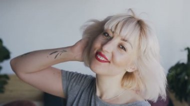 Kalıcı makyaj ve kırmızı ruj ile güzel ve gülümseyen kadın kameraya bakarak teşkil etmektedir. sarışın kız saç şehvetli portre üfleme. 120fps