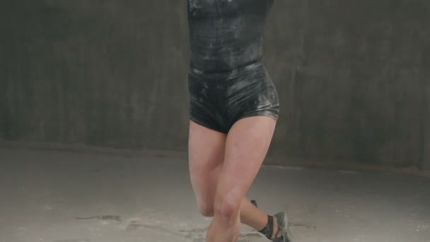 Beautiful expressive female dancer in black body suit is dancing at studio in clouds of smoke or white powder. Pretty young ballerina dancer dressed in body black t-shirt, shorts and ballerina shoes — Stock Video