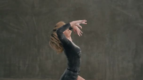黒のボディー スーツに身を包んだダンサーは 白い粉やスタジオで灰色の壁を背景に煙の雲にモダン ダンスを実行します 女性バレエ ダンサーの劇場 遅いステージ上で実行します — ストック動画