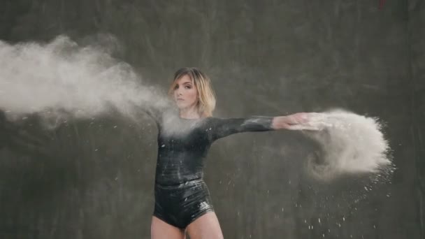 Danseuse au corps noir dansant gracieusement dans un nuage de poussière ou de poudre blanche sur fond gris à l'intérieur. Ballerine qui danse dans la fumée de poussière blanche au studio — Video