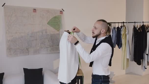Tailor working and dancing at work, measures the long sleeve white jacket using tape, writes down the numbers into his notepad. Modern, creative fashion studio. Trendy clothes, new collection, fashion — Stock Video