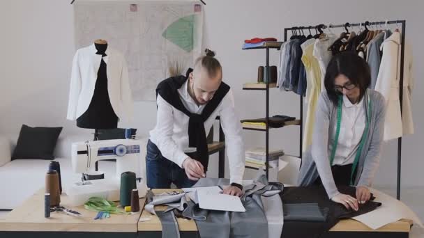 Дизайнер одежды и портниха разрабатывает новую коллекцию одежды в современном маленьком ателье. Успешное завершение рабочего дня. Модные дизайнеры сосредоточены на своей работе — стоковое видео