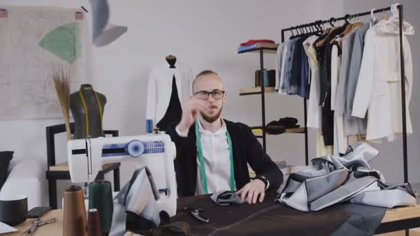 El sastre cansado y diseñador de moda con tela en sus manos en el taller. Un sastre agotado. Sastre barbudo loco y cansado al final de la jornada laboral en su estudio de diseño de sastrería — Vídeos de Stock